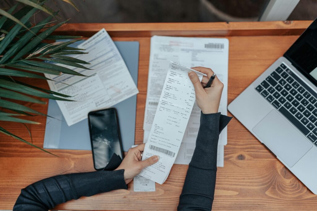 Person sorting receipts and paperwork beside a laptop and phone during a life admin session
