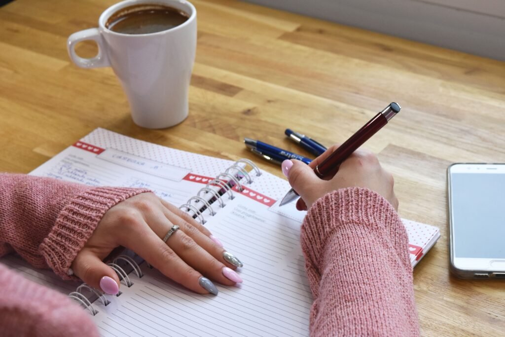 Person writing in a planner beside a coffee and phone