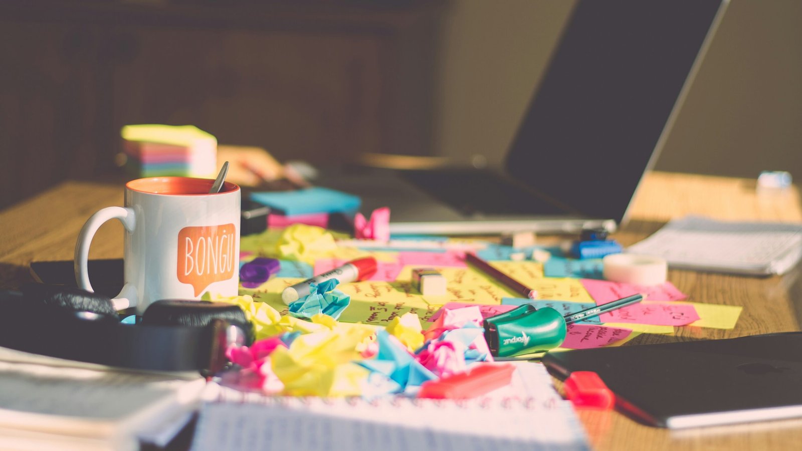 Cluttered desk with laptop, sticky notes, notebooks and coffee during a routine reset