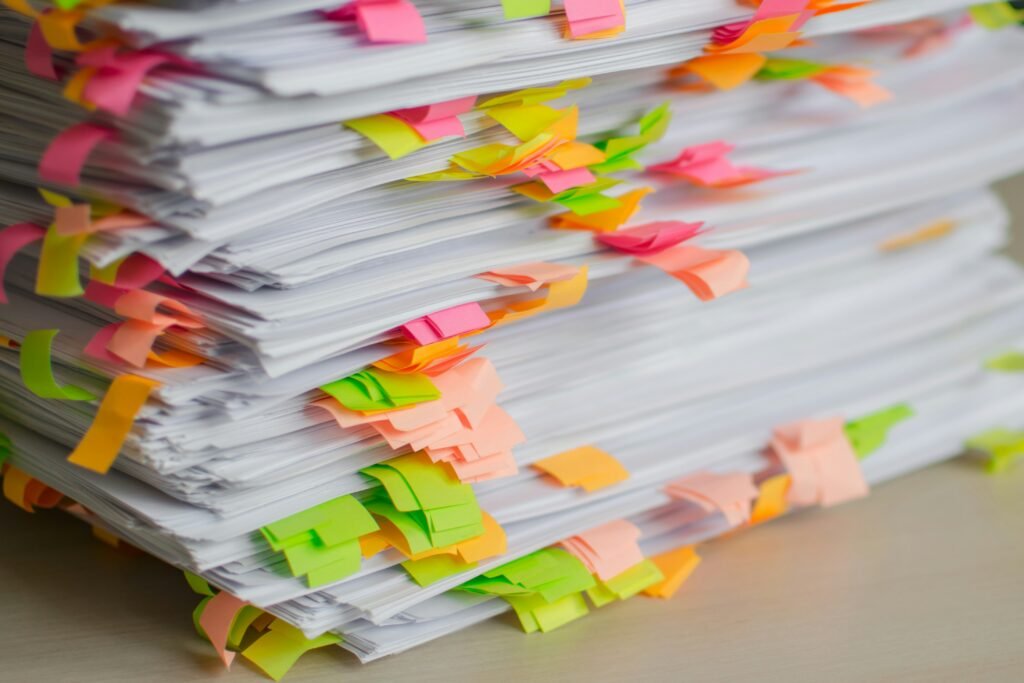 Stack of paperwork covered in colourful sticky notes representing unfinished life admin tasks